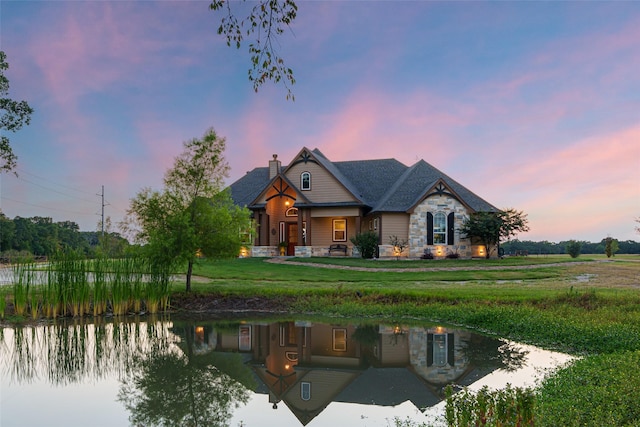 view of front of property featuring a water view, stone siding, a chimney, and a yard