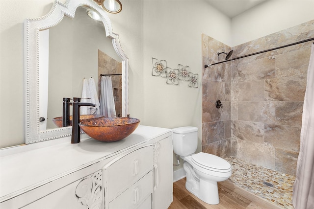 full bathroom with a tile shower, vanity, wood finished floors, and toilet