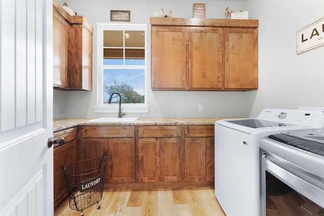 laundry area with cabinet space, a sink, washer and clothes dryer, and light wood finished floors