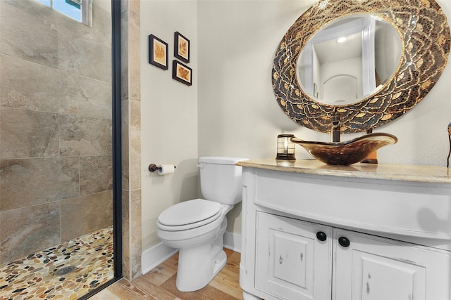 full bathroom featuring toilet, wood finished floors, vanity, baseboards, and tiled shower