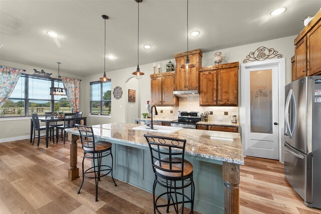 kitchen featuring light wood-style flooring, a sink, appliances with stainless steel finishes, decorative backsplash, and brown cabinetry