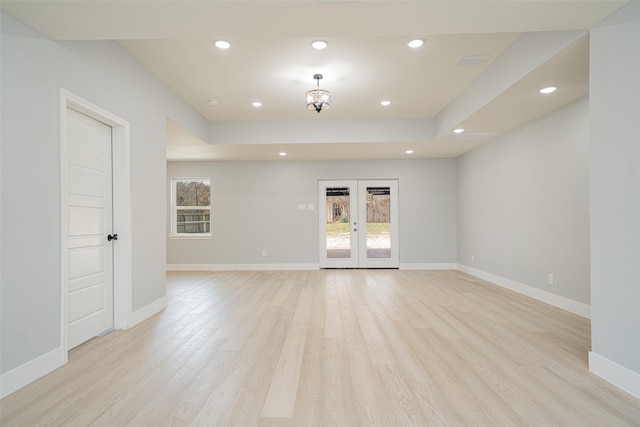 empty room featuring light wood finished floors, baseboards, a raised ceiling, french doors, and recessed lighting