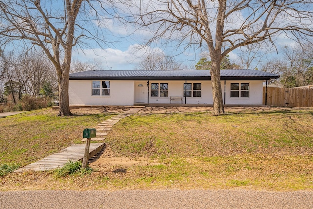 ranch-style home with a front yard, metal roof, brick siding, and fence