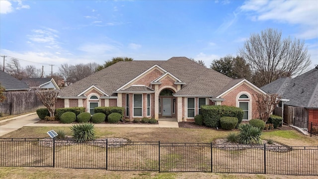 view of front of house featuring brick siding, a fenced front yard, a front yard, and a shingled roof