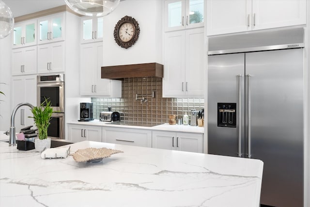 kitchen with stainless steel appliances, a sink, white cabinets, tasteful backsplash, and glass insert cabinets