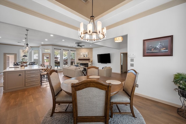 dining room with ornamental molding, a tray ceiling, a fireplace, and wood finished floors