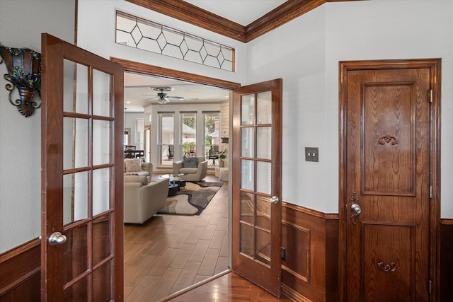 foyer entrance with ceiling fan, a wainscoted wall, wood finished floors, ornamental molding, and french doors