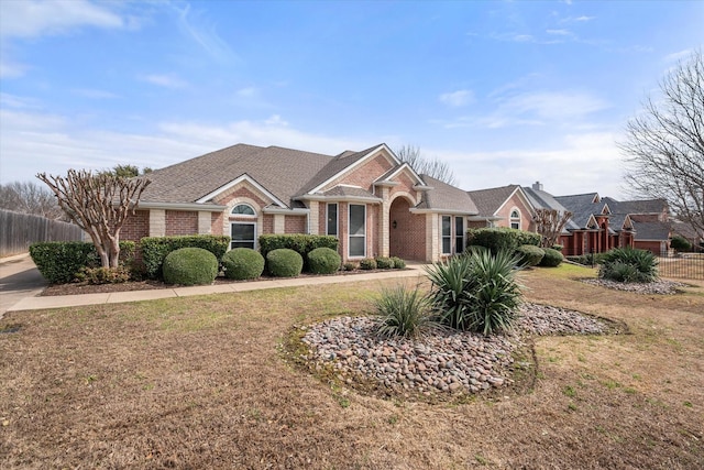 view of front of house featuring a front yard, brick siding, fence, and roof with shingles