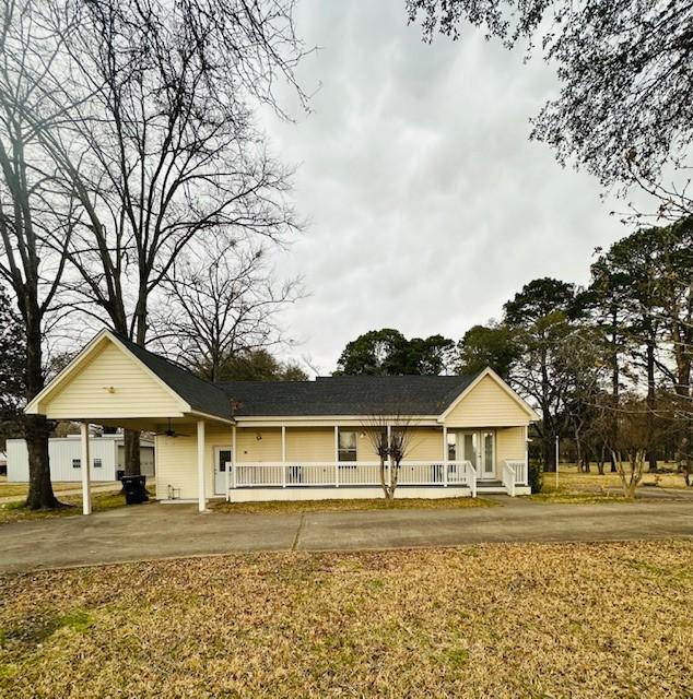 single story home featuring driveway, a porch, a front lawn, and an attached carport