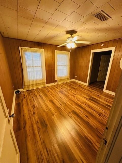 unfurnished room with wood walls, wood finished floors, visible vents, and baseboards