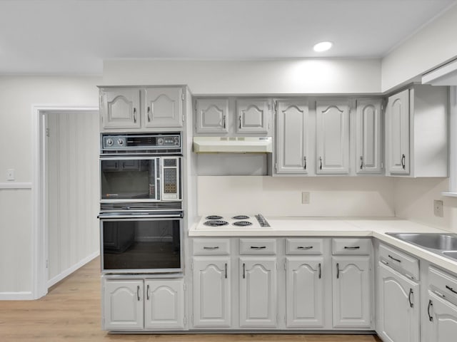 kitchen featuring light wood-style flooring, under cabinet range hood, dobule oven black, light countertops, and white electric stovetop