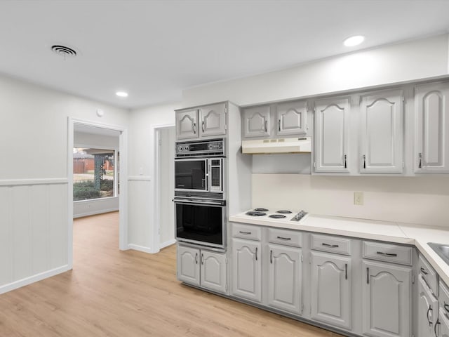 kitchen featuring light wood finished floors, visible vents, multiple ovens, gray cabinetry, and under cabinet range hood