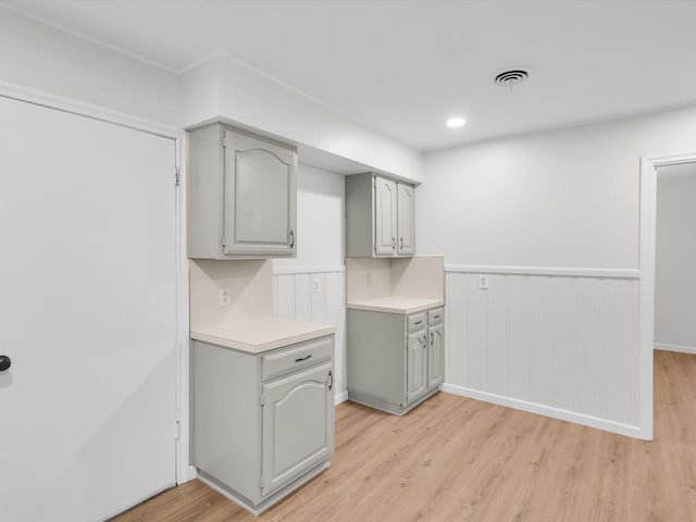 kitchen featuring a wainscoted wall, visible vents, light wood-style floors, light countertops, and gray cabinets