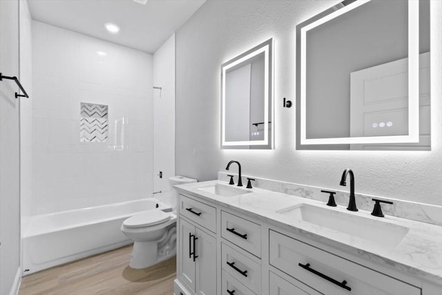 full bathroom featuring toilet, a textured wall, a sink, and wood finished floors