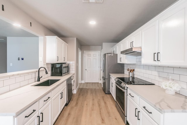 kitchen featuring stainless steel appliances, white cabinets, a sink, light wood-type flooring, and under cabinet range hood