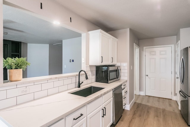 kitchen with light wood finished floors, stainless steel appliances, backsplash, white cabinets, and a sink