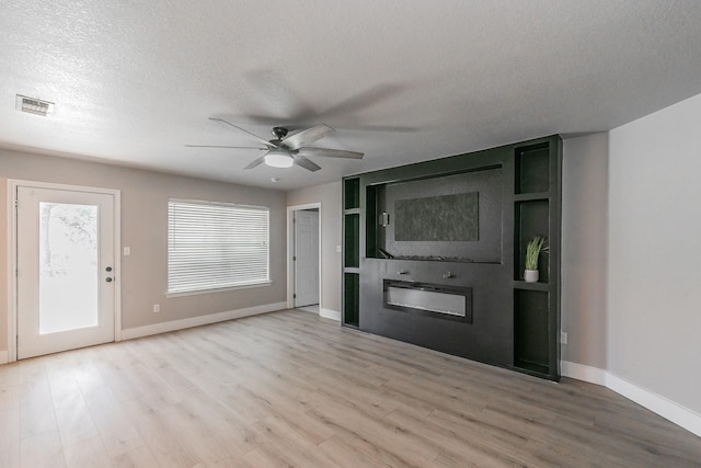 entryway featuring visible vents, a ceiling fan, a textured ceiling, light wood-style floors, and a fireplace