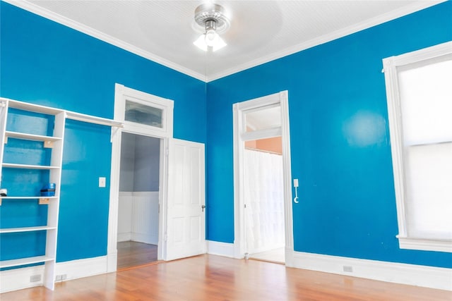 empty room with ceiling fan, baseboards, wood finished floors, and crown molding