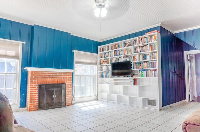 tiled living area featuring visible vents, a ceiling fan, a brick fireplace, and crown molding