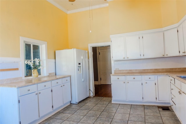 kitchen with visible vents, crown molding, wainscoting, white refrigerator with ice dispenser, and a high ceiling