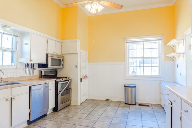 kitchen featuring a wainscoted wall, light countertops, appliances with stainless steel finishes, white cabinets, and a sink