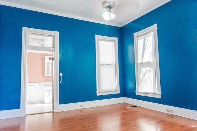 spare room with a ceiling fan, baseboards, wood finished floors, visible vents, and ornamental molding