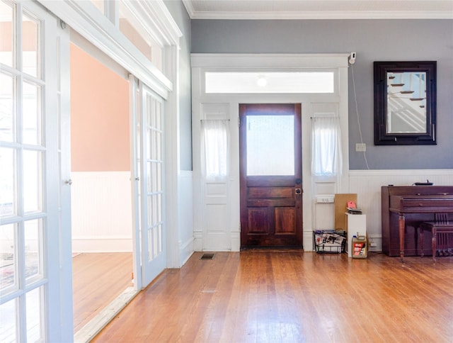 foyer entrance with a wainscoted wall, crown molding, visible vents, and wood finished floors