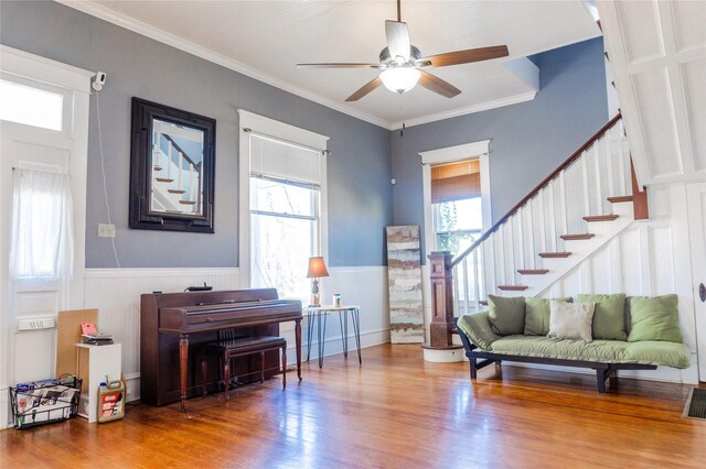 living area featuring wood finished floors, a wainscoted wall, ceiling fan, stairs, and ornamental molding