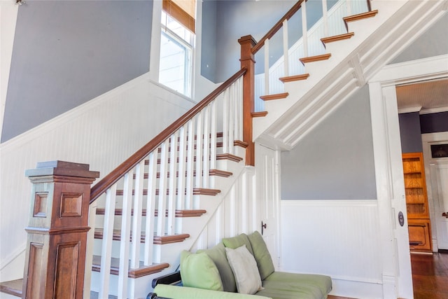 stairway with wainscoting, a towering ceiling, and wood finished floors