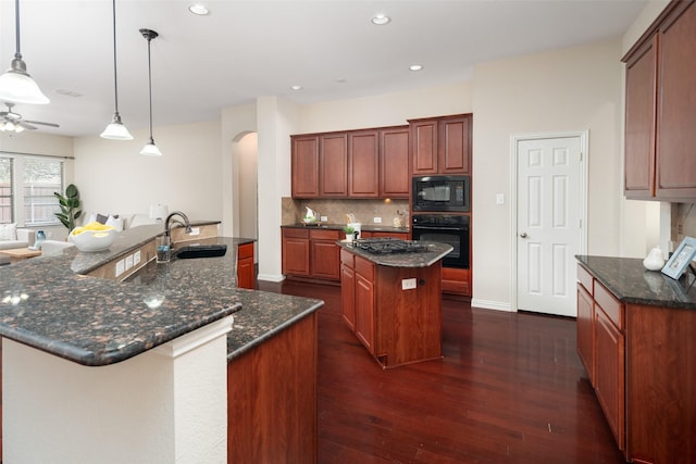 kitchen featuring arched walkways, a large island, backsplash, a sink, and black appliances