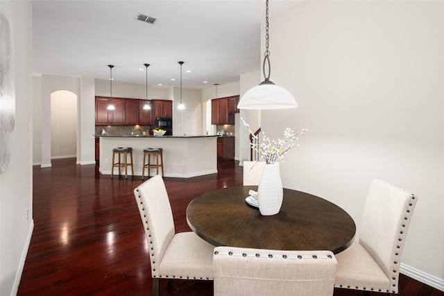 dining room with baseboards, visible vents, arched walkways, and dark wood-type flooring