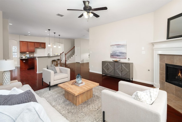 living room with stairs, visible vents, dark wood-style flooring, and a tile fireplace