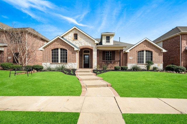 view of front facade with brick siding, a shingled roof, covered porch, a front yard, and stone siding