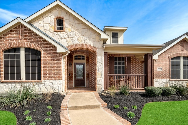 entrance to property featuring stone siding, a porch, and brick siding