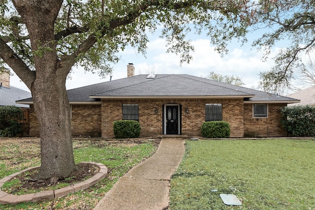 ranch-style home with a shingled roof, a front yard, a chimney, and brick siding