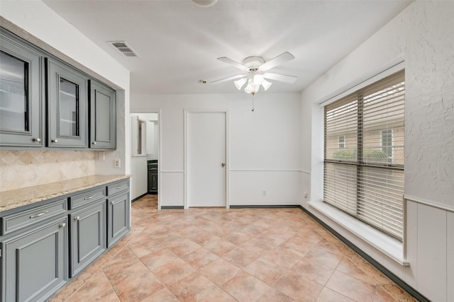 kitchen featuring ceiling fan, visible vents, gray cabinets, light stone countertops, and glass insert cabinets