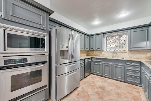 kitchen with backsplash, stainless steel appliances, a sink, and gray cabinetry