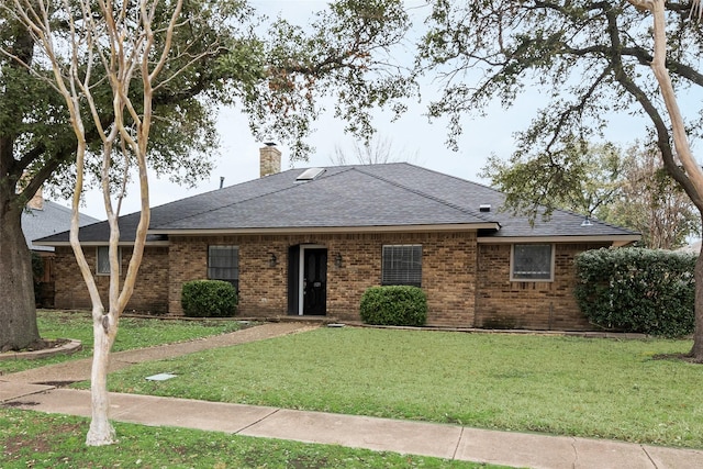 single story home featuring a shingled roof, a front yard, a chimney, and brick siding