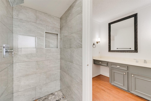 bathroom featuring a tile shower, wood finished floors, and vanity