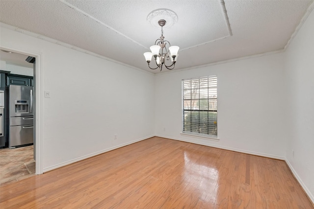 unfurnished room featuring baseboards, a textured ceiling, light wood finished floors, and an inviting chandelier