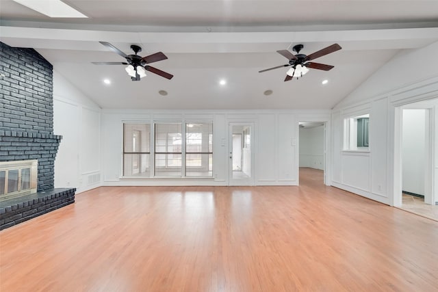 unfurnished living room featuring ceiling fan, a brick fireplace, light wood-style flooring, and a decorative wall