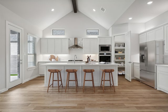 kitchen featuring a kitchen island with sink, visible vents, light countertops, appliances with stainless steel finishes, and wall chimney exhaust hood