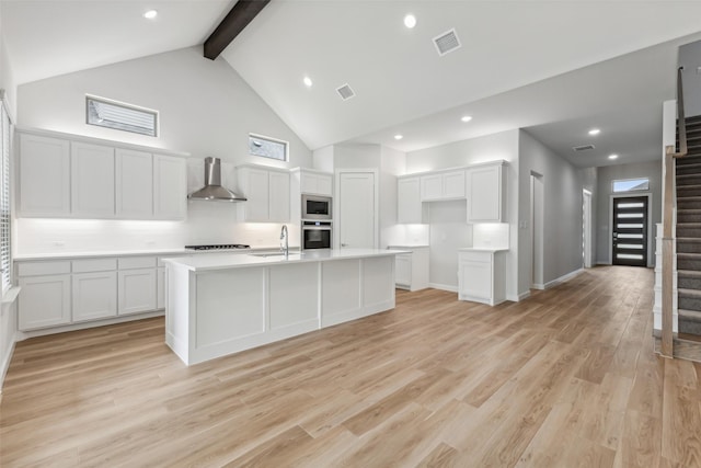 kitchen featuring light wood-style floors, wall chimney exhaust hood, visible vents, and appliances with stainless steel finishes