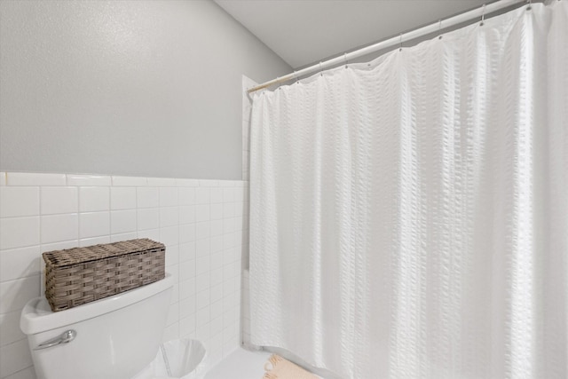 full bath featuring toilet, a wainscoted wall, tile walls, and a shower with curtain