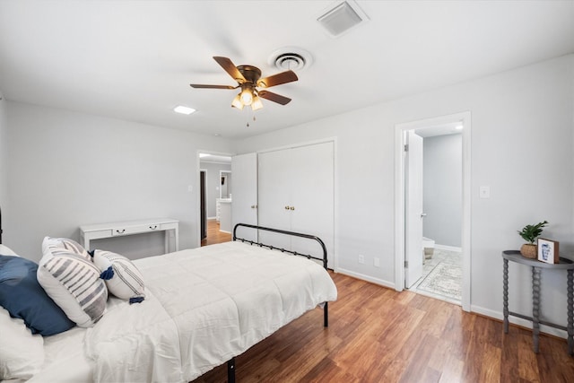 bedroom featuring visible vents, ensuite bathroom, baseboards, and wood finished floors