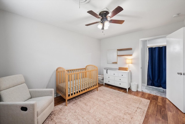 bedroom with a nursery area, ceiling fan, and wood finished floors