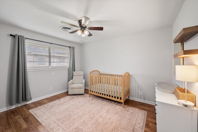 bedroom featuring a crib, baseboards, visible vents, and wood finished floors