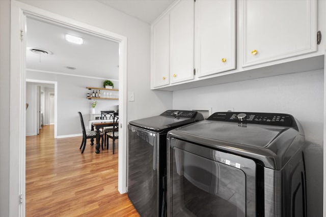 clothes washing area with light wood finished floors, washing machine and clothes dryer, cabinet space, and baseboards