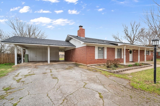 view of front of house with a chimney, aphalt driveway, fence, a carport, and brick siding