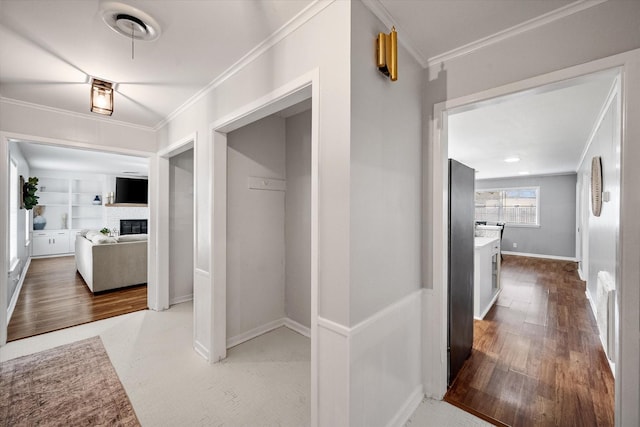 hallway featuring ornamental molding, baseboards, built in shelves, and wood finished floors